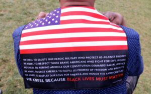 A man drapes the Black Lives Must Matter Kneel Flag down over his back while kneeling